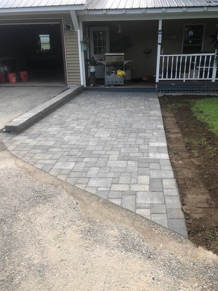 New paver driveway leading to a covered front porch with a garage on the left