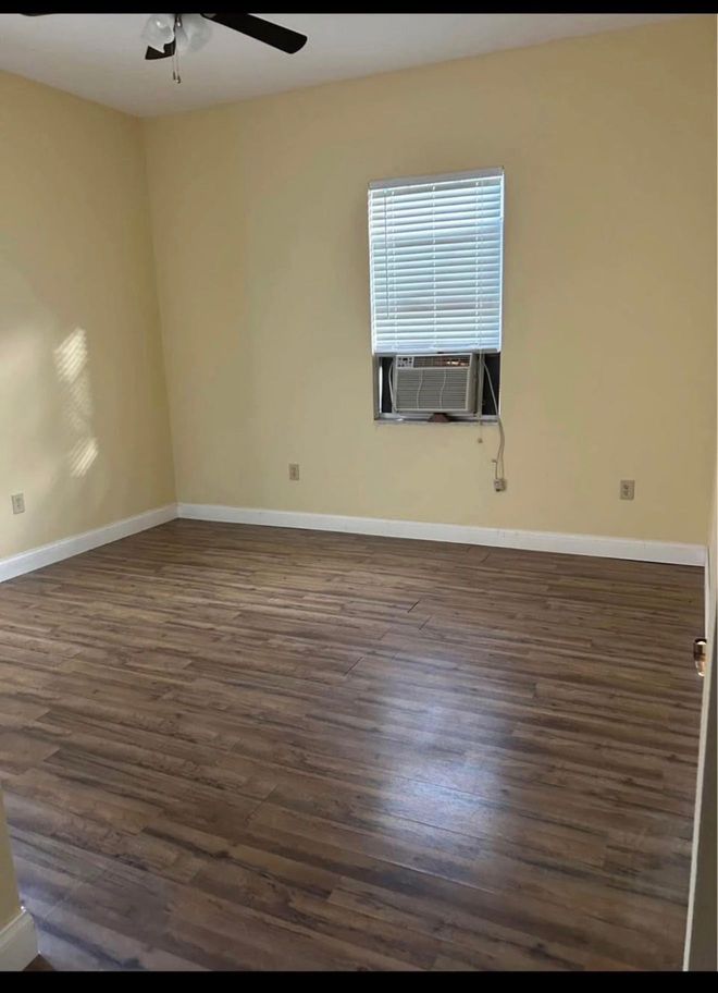 Empty room with wood floors, beige walls, and a window air conditioner under a small window.