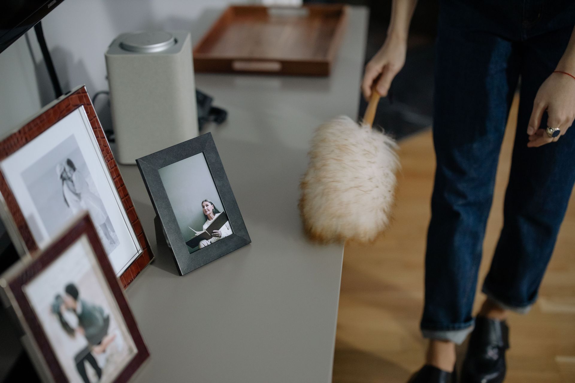 Framed photos on a table as a person dusts them with a feather duster in a home interior