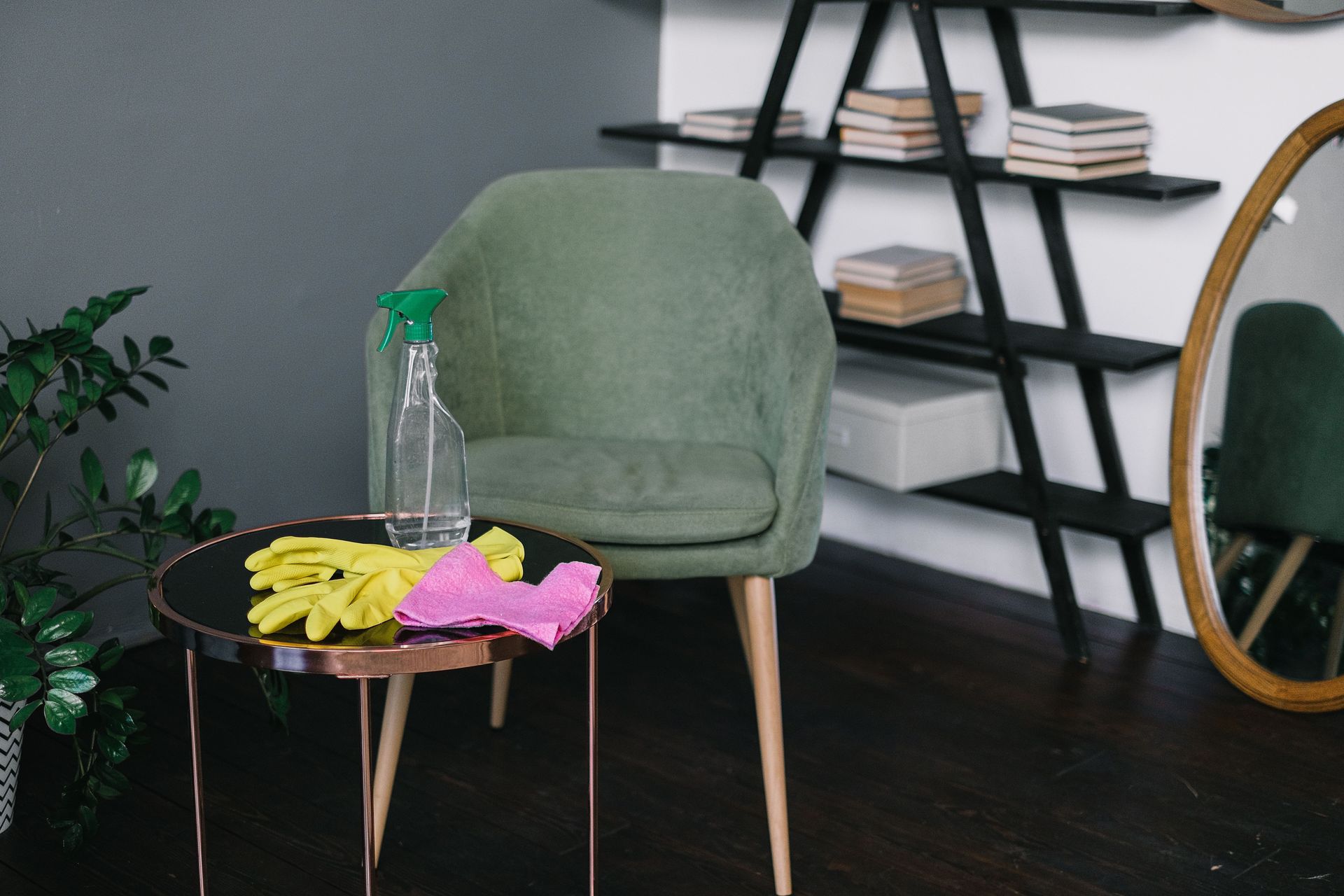 Green chair beside a small table with gloves and spray bottle in a cozy room with shelves and a mirror