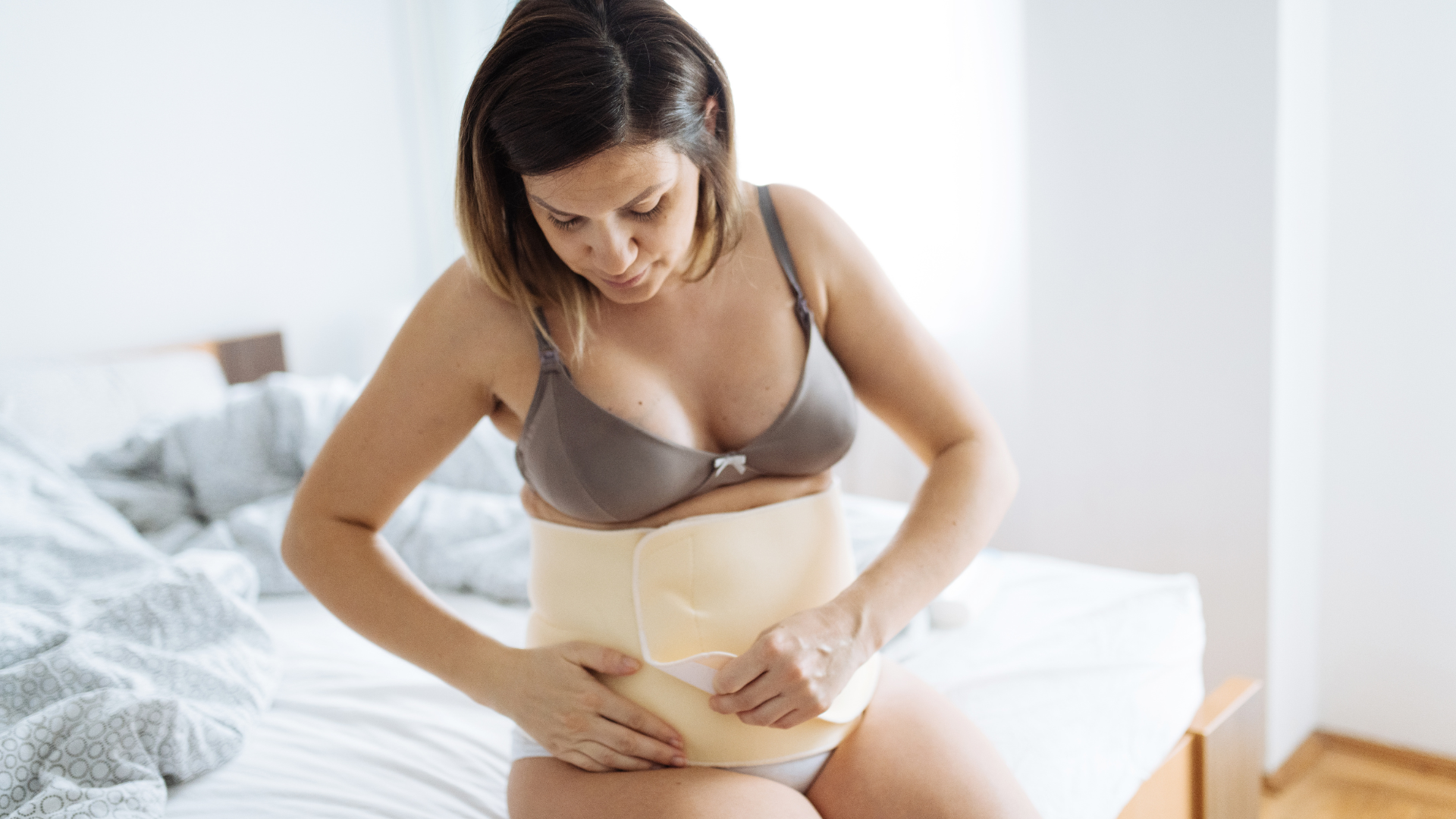 Woman putting on brace on stomach after pregnancy