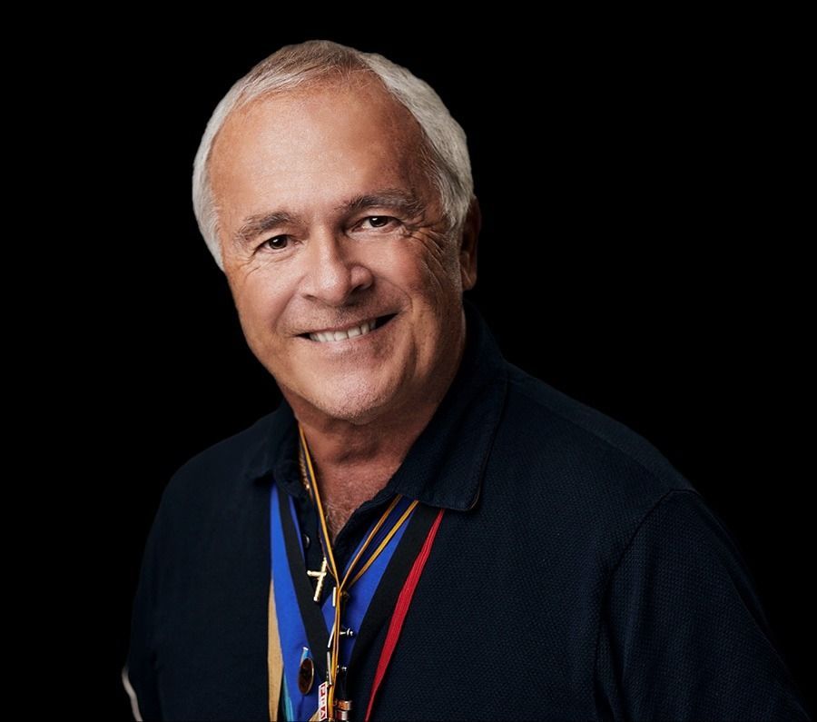 Smiling man in a dark shirt with colorful lanyards against a black background
