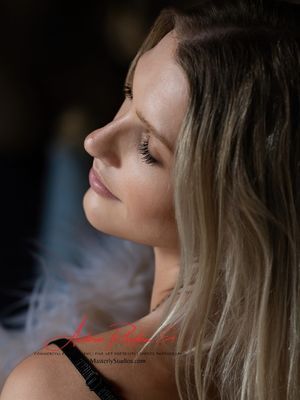 Close-up side profile of a person with blonde hair, eyes closed, against a dark background.