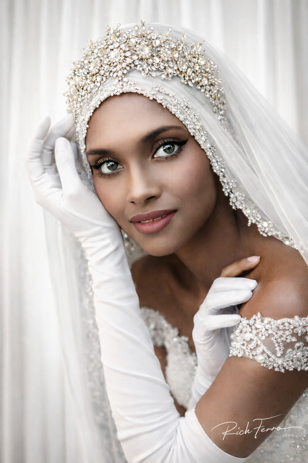 Bride in a jeweled veil and white gloves, posing softly against a light curtain backdrop.