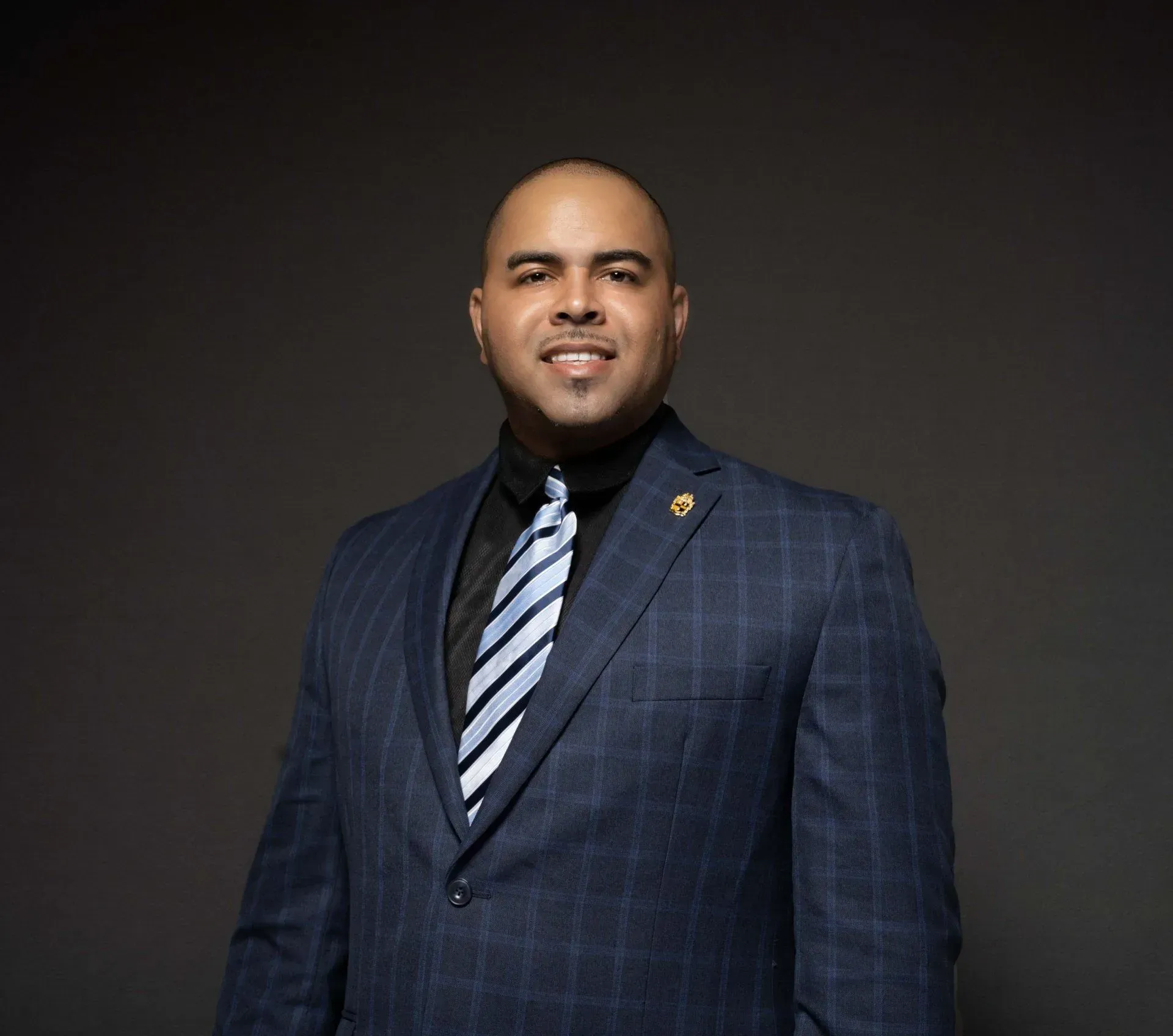 Portrait of a man in a dark blue suit and striped tie against a dark background