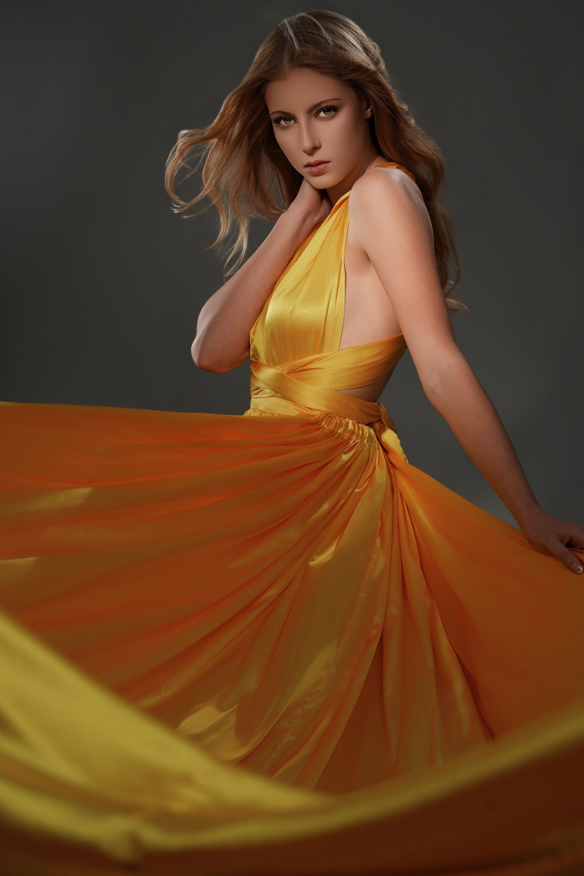 Woman in a flowing yellow-orange gown posing against a dark studio background