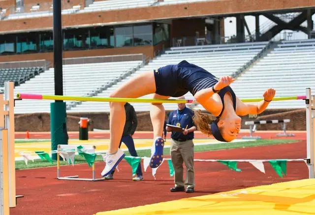 Athlete clearing a high jump bar on a track field, with a coach standing nearby