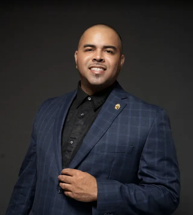 Man in a navy checkered suit smiling against a dark studio background