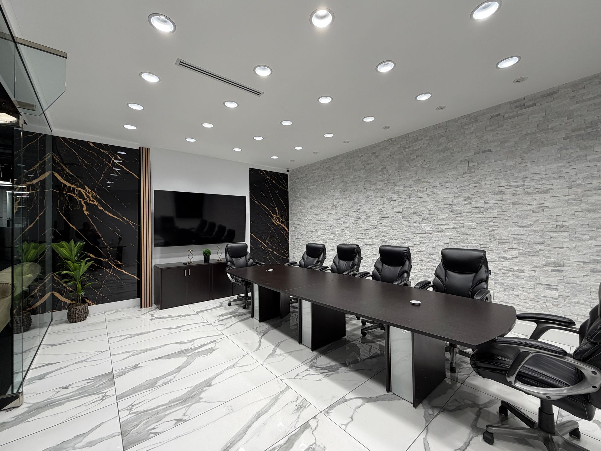 Modern conference room with long black table, office chairs, wall-mounted TV, and marble floor.