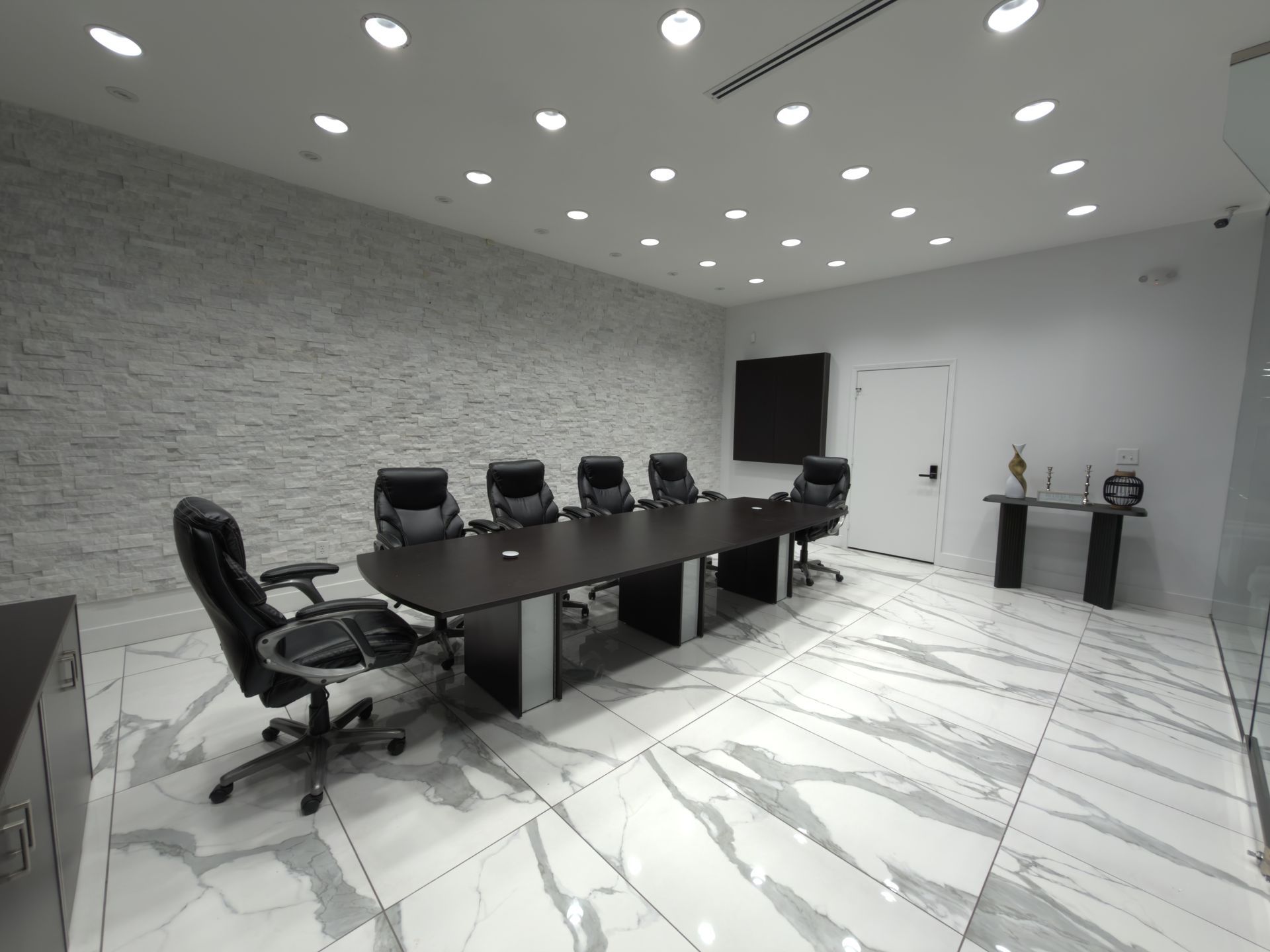 Modern conference room with black table, rolling chairs, gray walls, and marble floor
