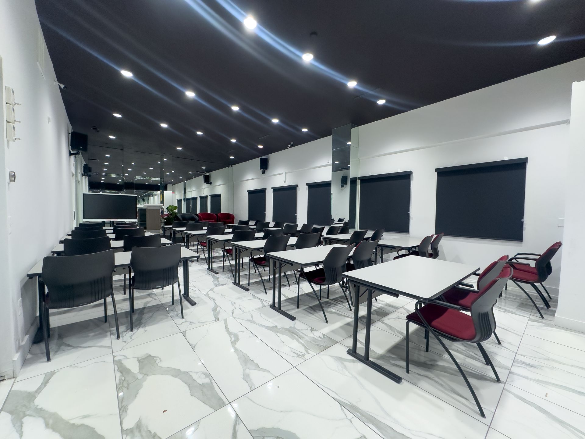 Empty modern classroom with desks and chairs, white walls, black ceiling, and bright recessed lights