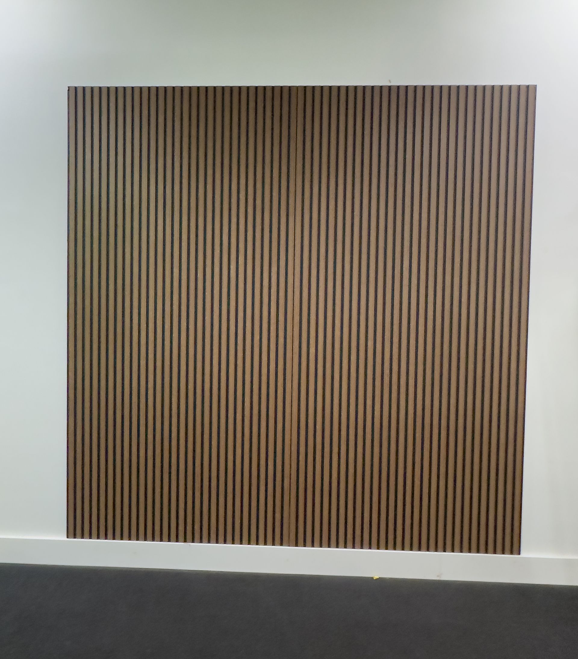 Vertical striped wall art on a white wall above a dark floor trim