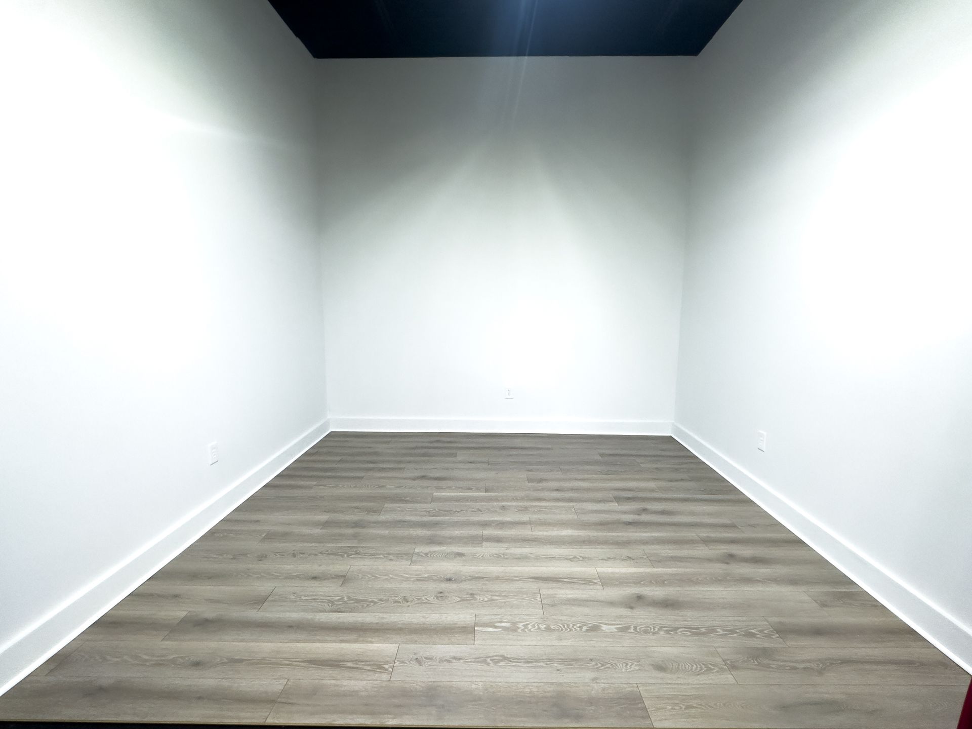 Empty white room with gray wood flooring and dark ceiling recess