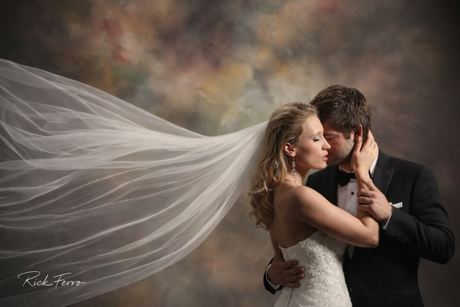 Bride and groom embracing, with the bride’s veil flowing dramatically against a soft studio backdrop.