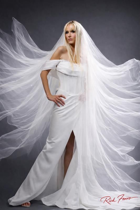 Woman in a white flowing gown and veil posing against a gray studio backdrop