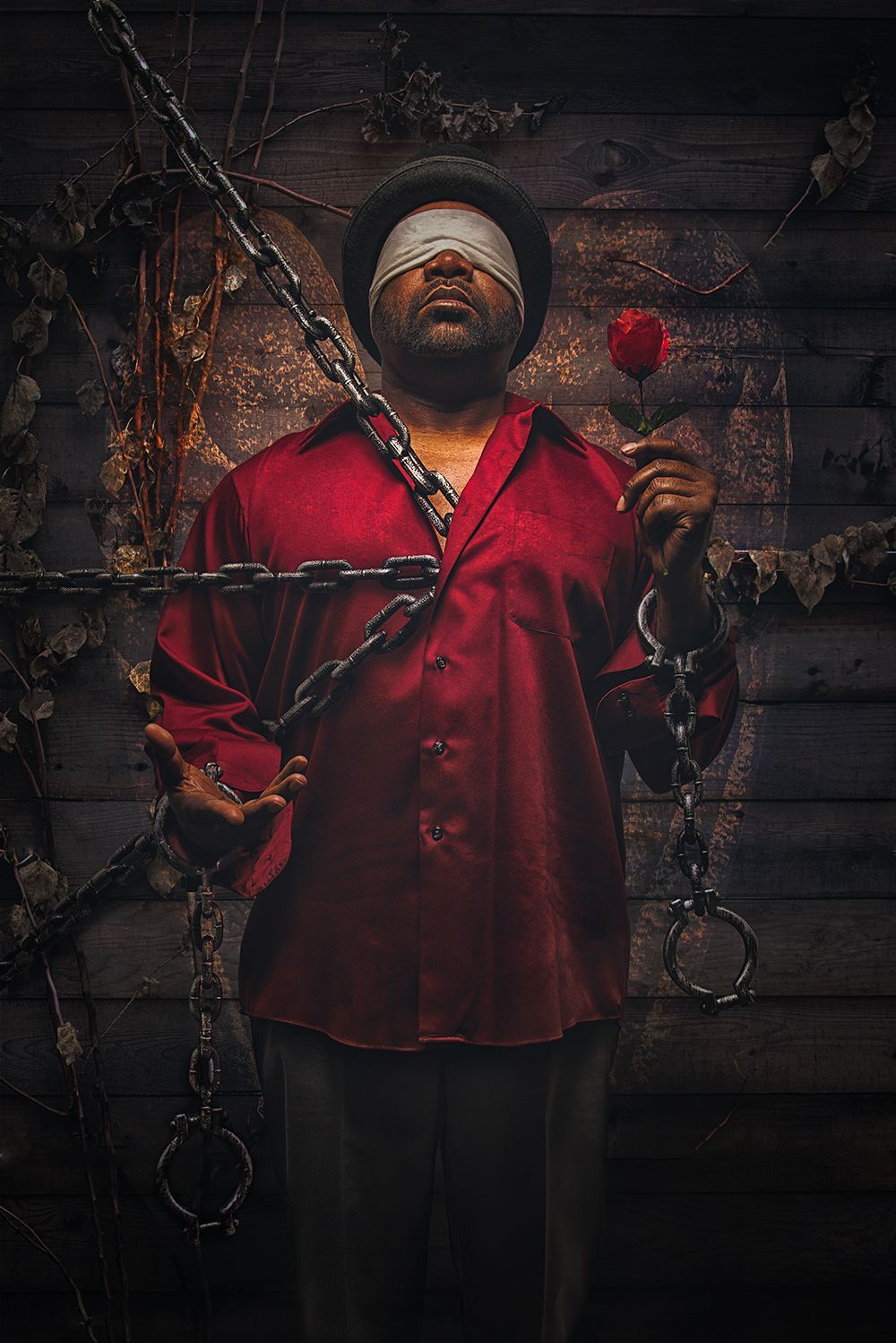 Bloodied man in red shirt hanging from chains against a dark wooden wall