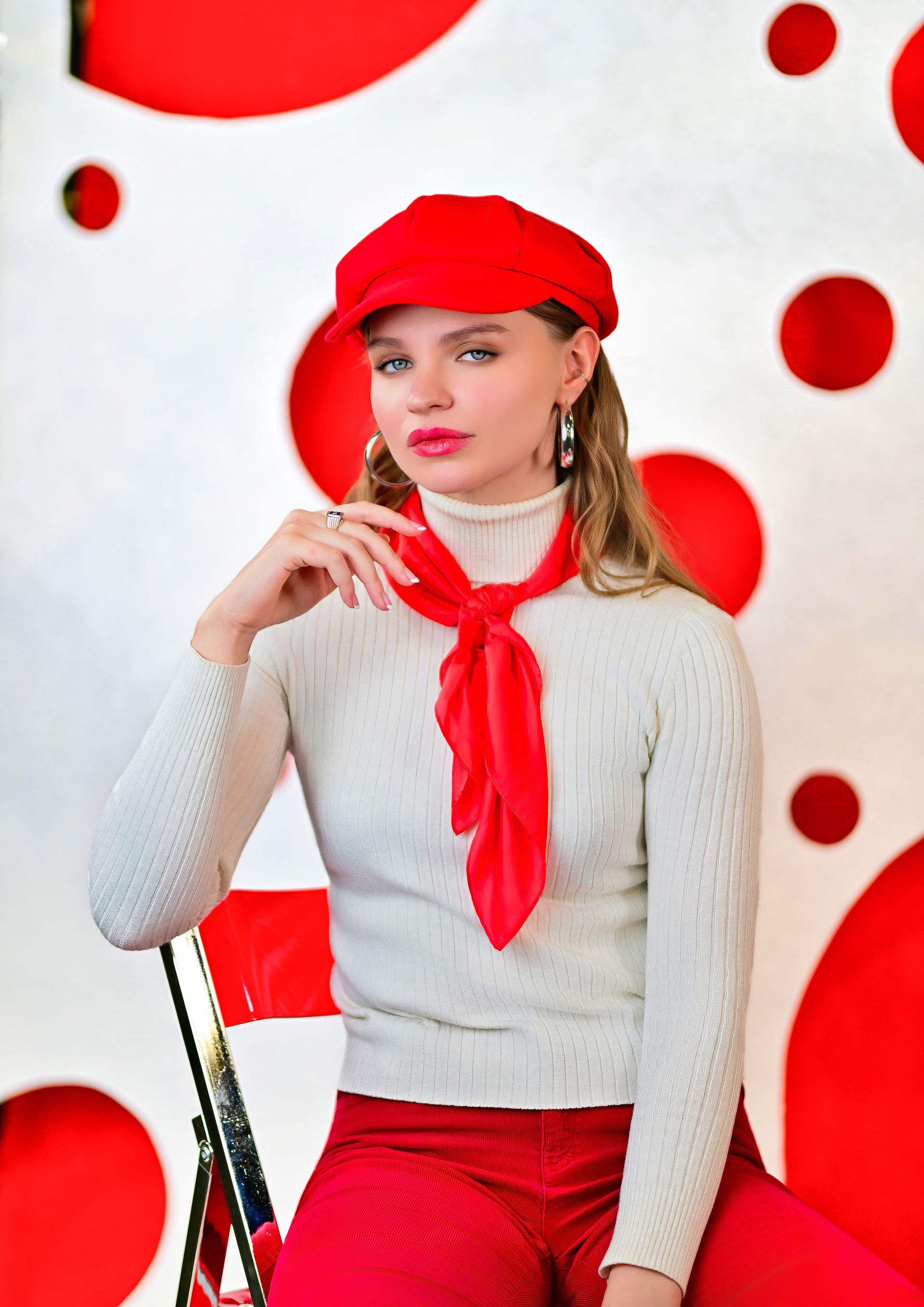 Woman in red beret and scarf posing against a white wall with red polka dots.