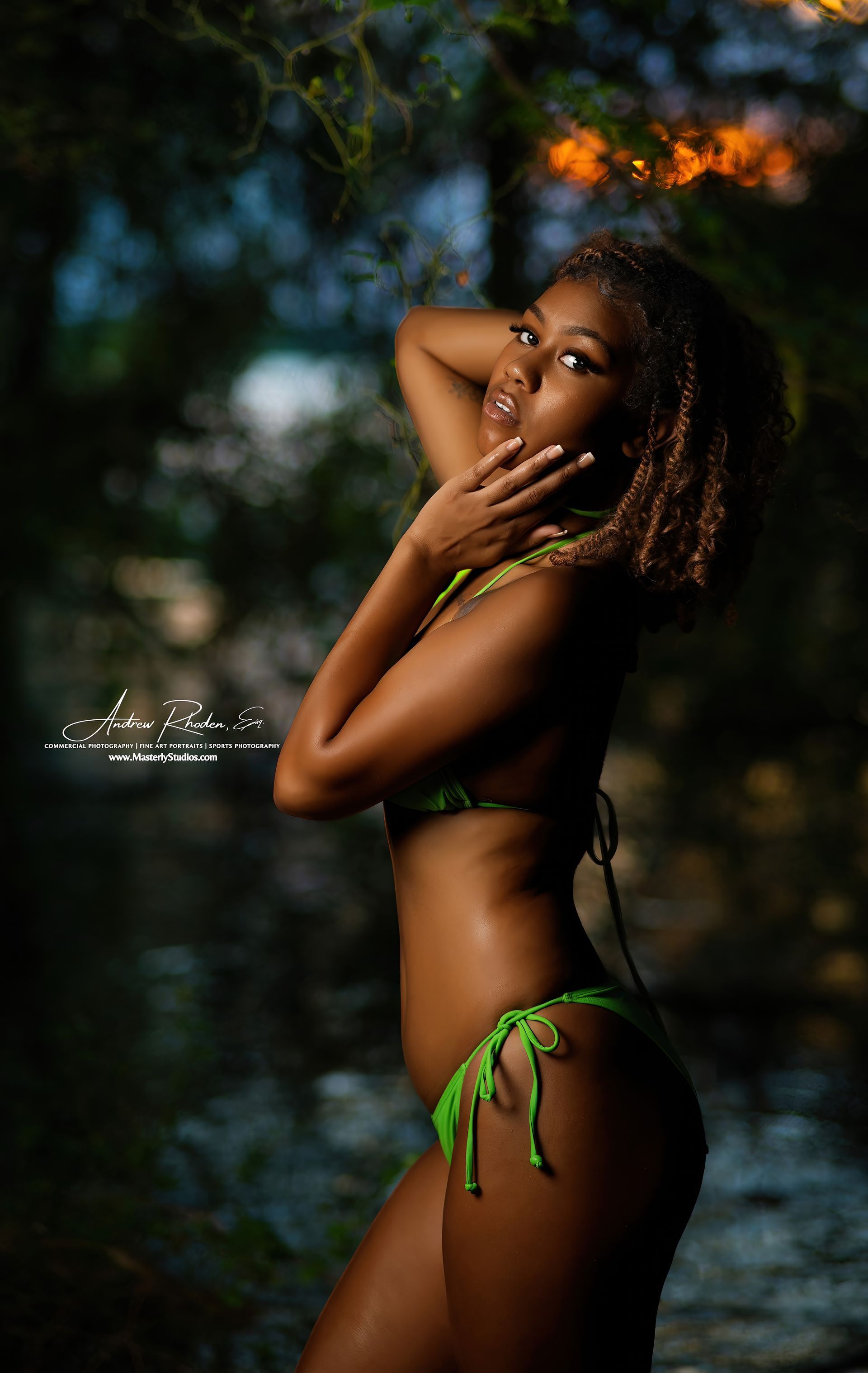 Woman posing in a green bikini against a dark, blurred outdoor background