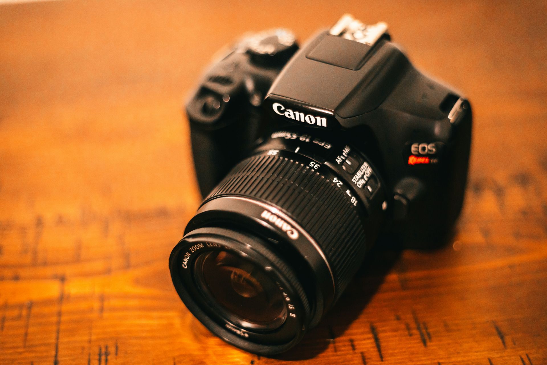 Canon EOS camera with lens on a wooden table, warmly lit