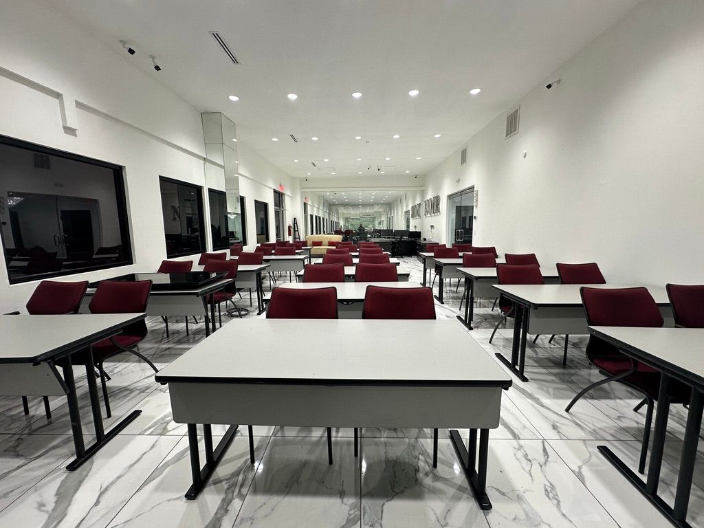 Bright classroom or lecture hall with rows of tables and maroon chairs under ceiling lights