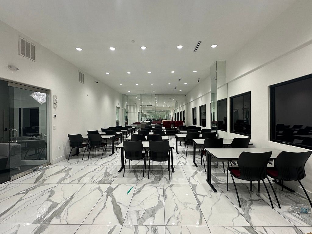 Bright modern dining hall with black chairs, white marble floor, and long tables under recessed ceiling lights