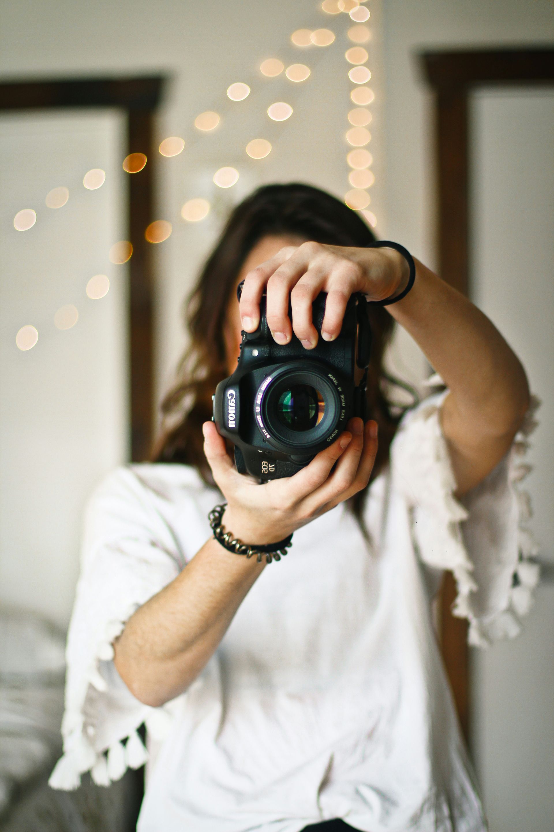 Person holding a camera up to their face indoors, with blurred string lights in the background
