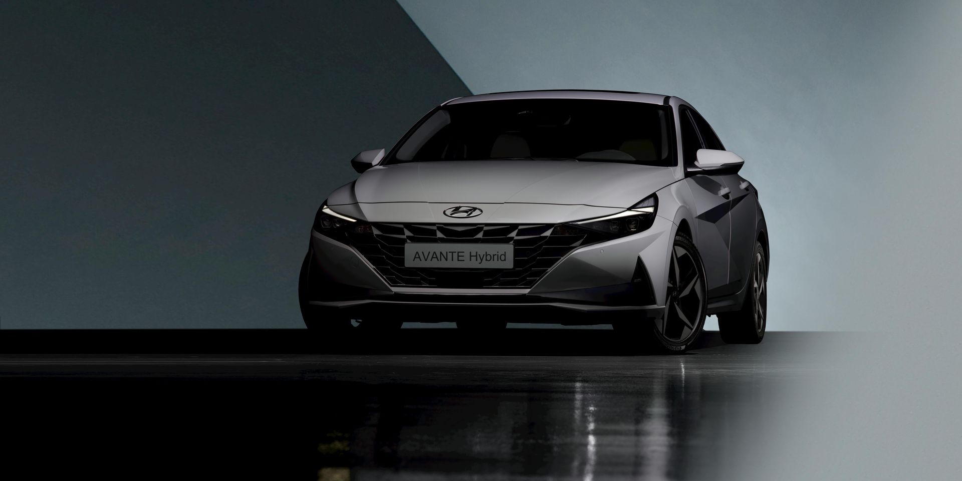 Sleek silver sports car on a dark studio floor, front view with dramatic lighting.