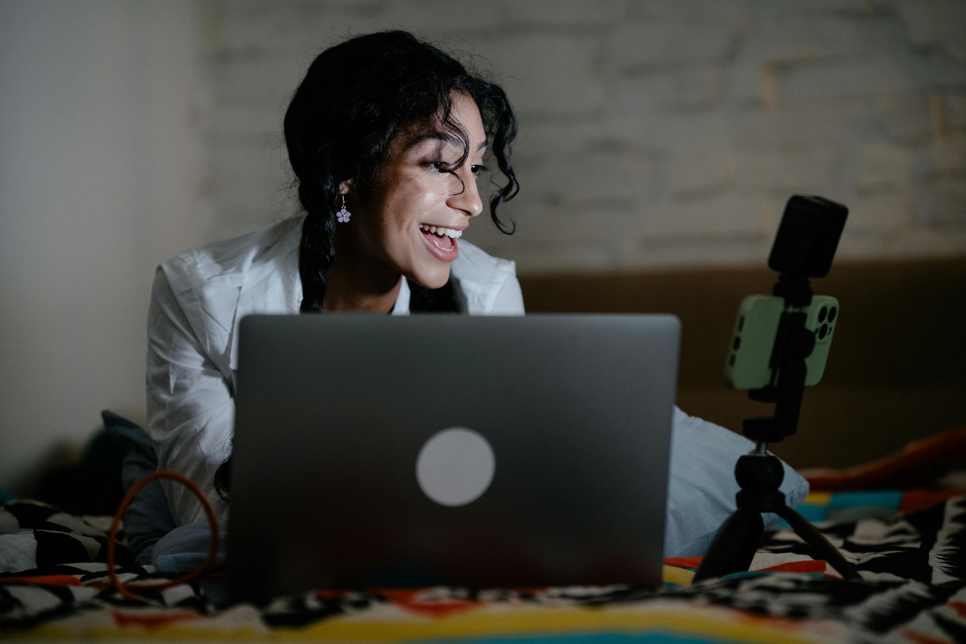 Woman smiling while recording at a laptop with a microphone on a table in a dimly lit room