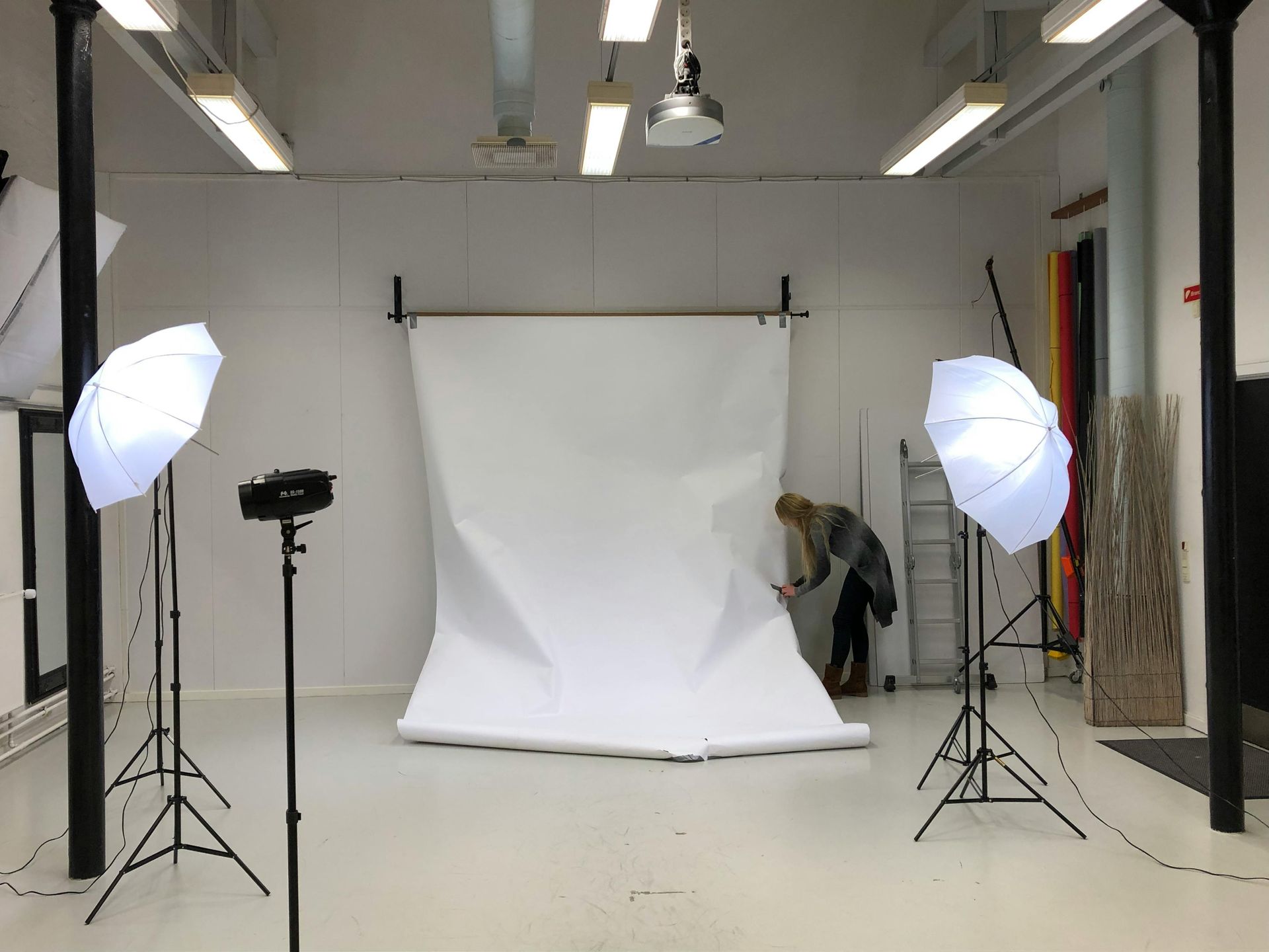 Photo studio with white backdrop, two softbox lights, and a person adjusting the backdrop.