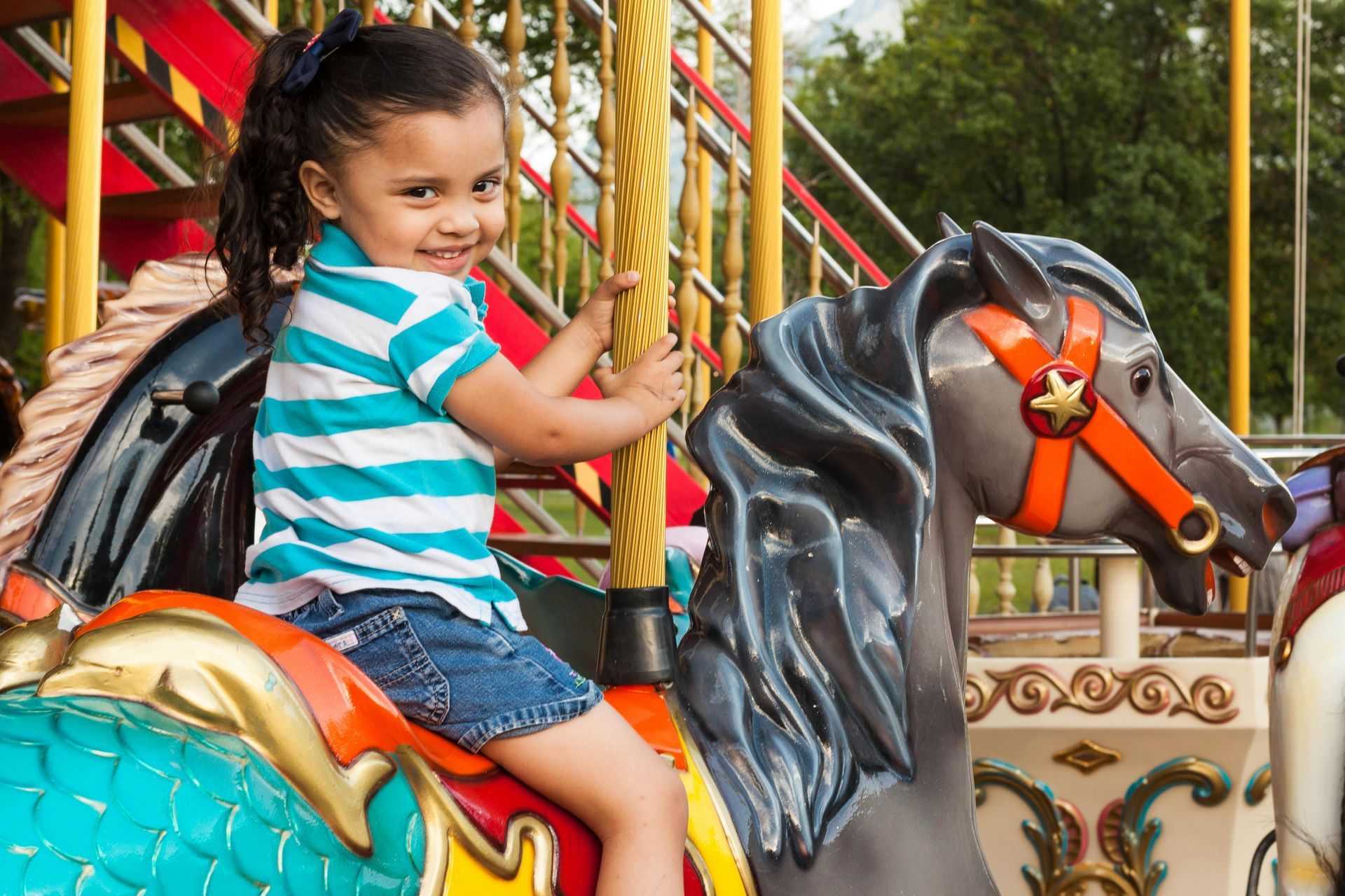 Smiling child riding a black carousel horse in a colorful playground