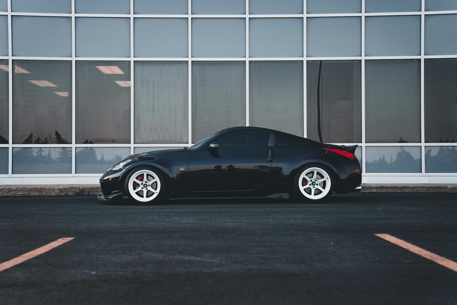 Black sports coupe parked in front of a glass-front building at dusk