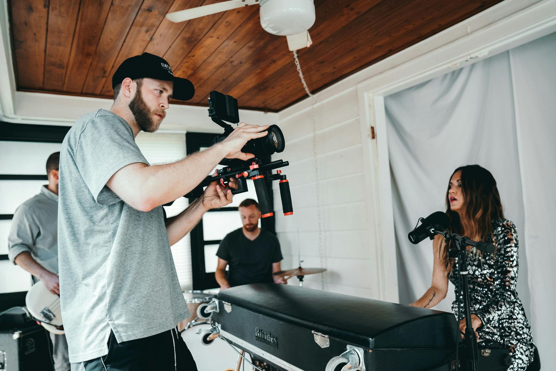 Video crew filming an interview in a bright room, with a camera operator and a seated subject beside a massage table