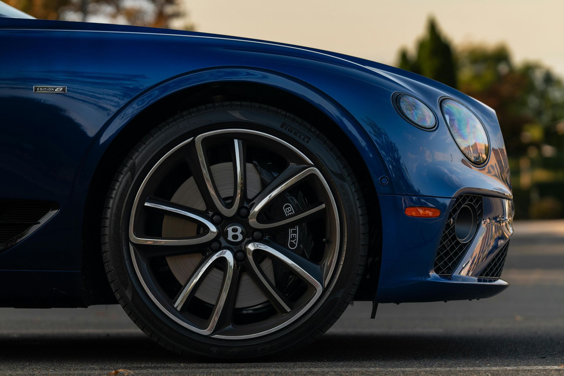 Blue sports car with black wheels and chrome grille driving on a road