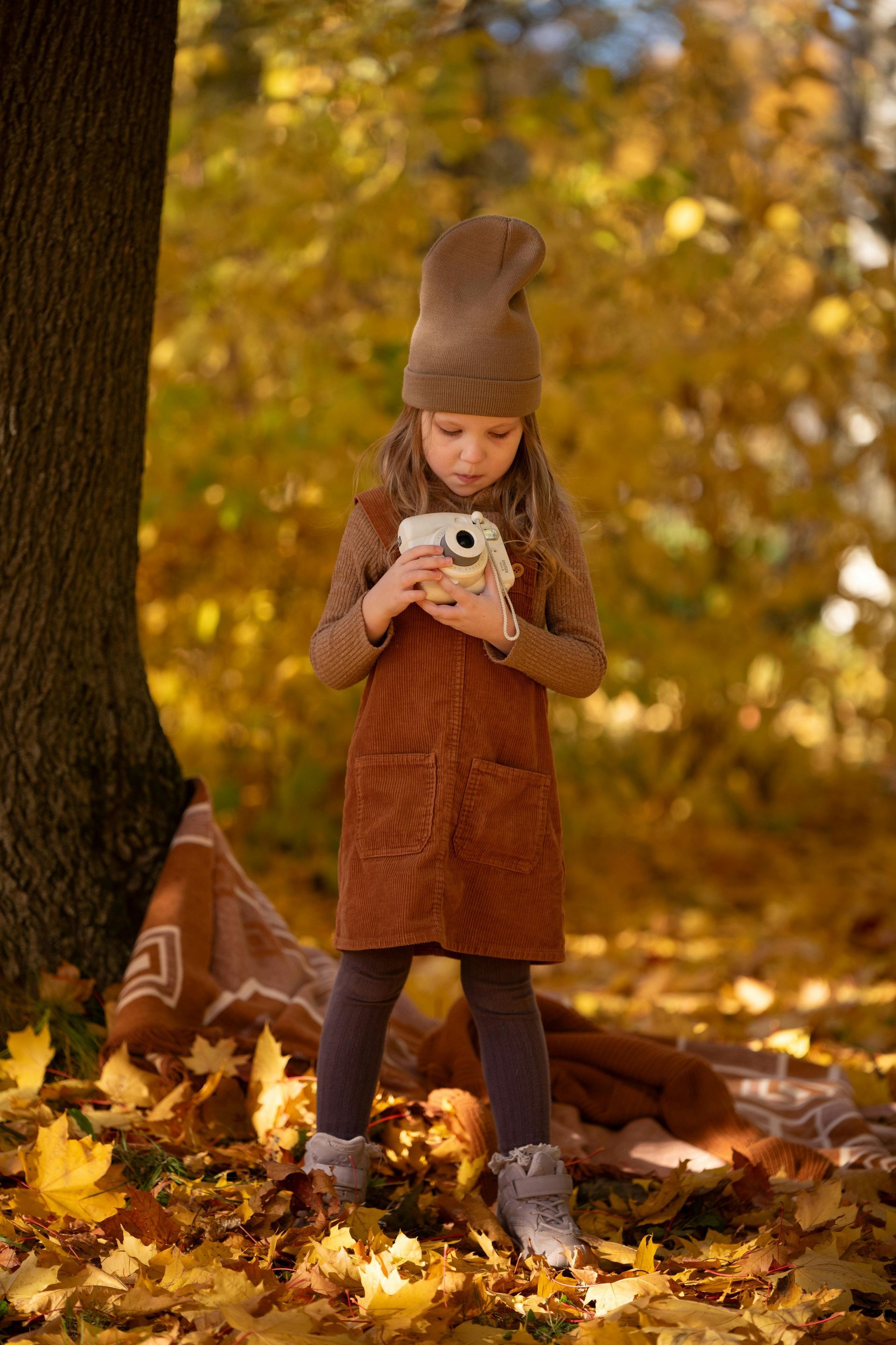 Young child in brown coat and knit hat holding a small owl in an autumn forest