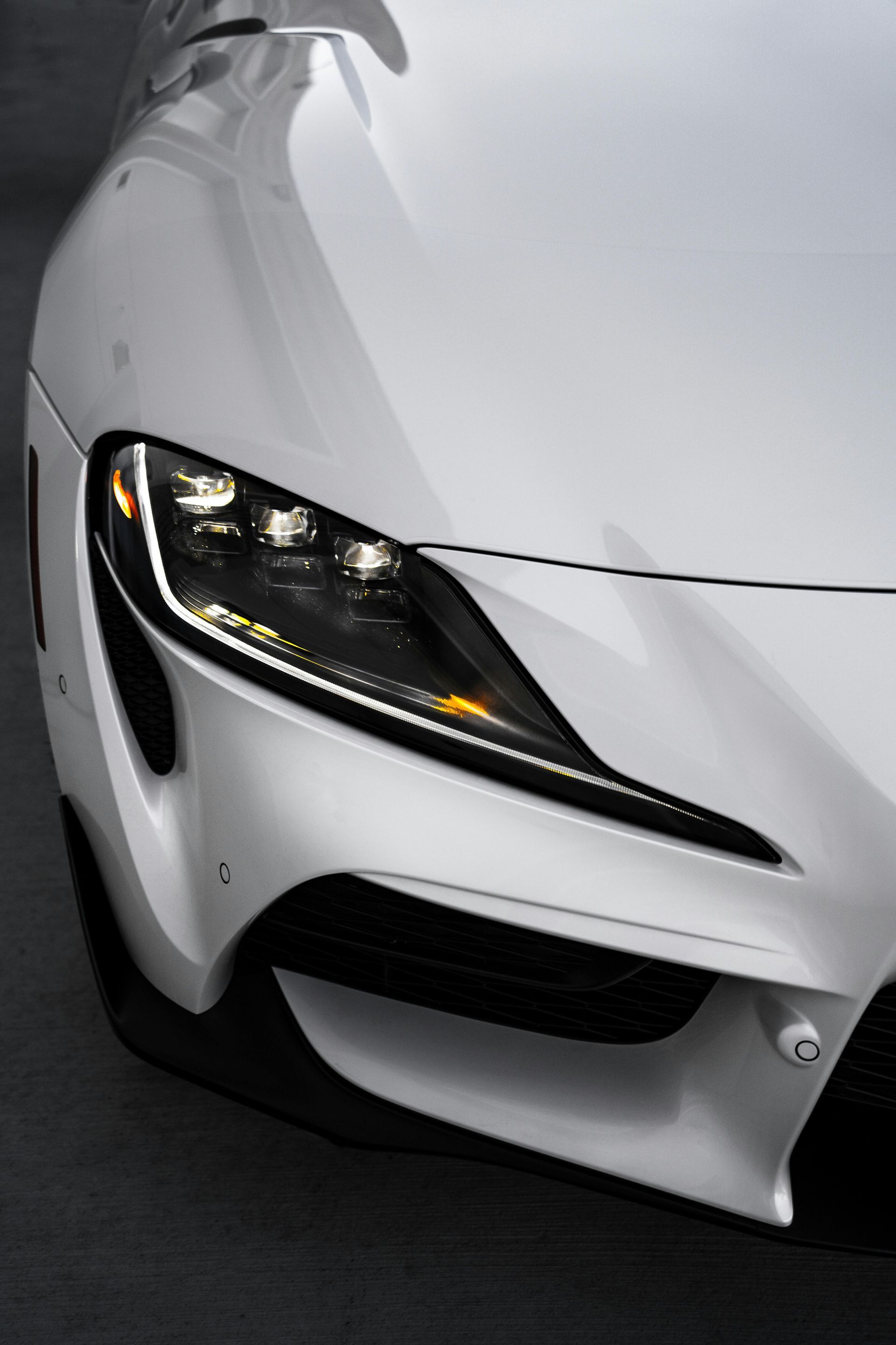 Front view of a white sports car with a sleek black headlight on a dark background