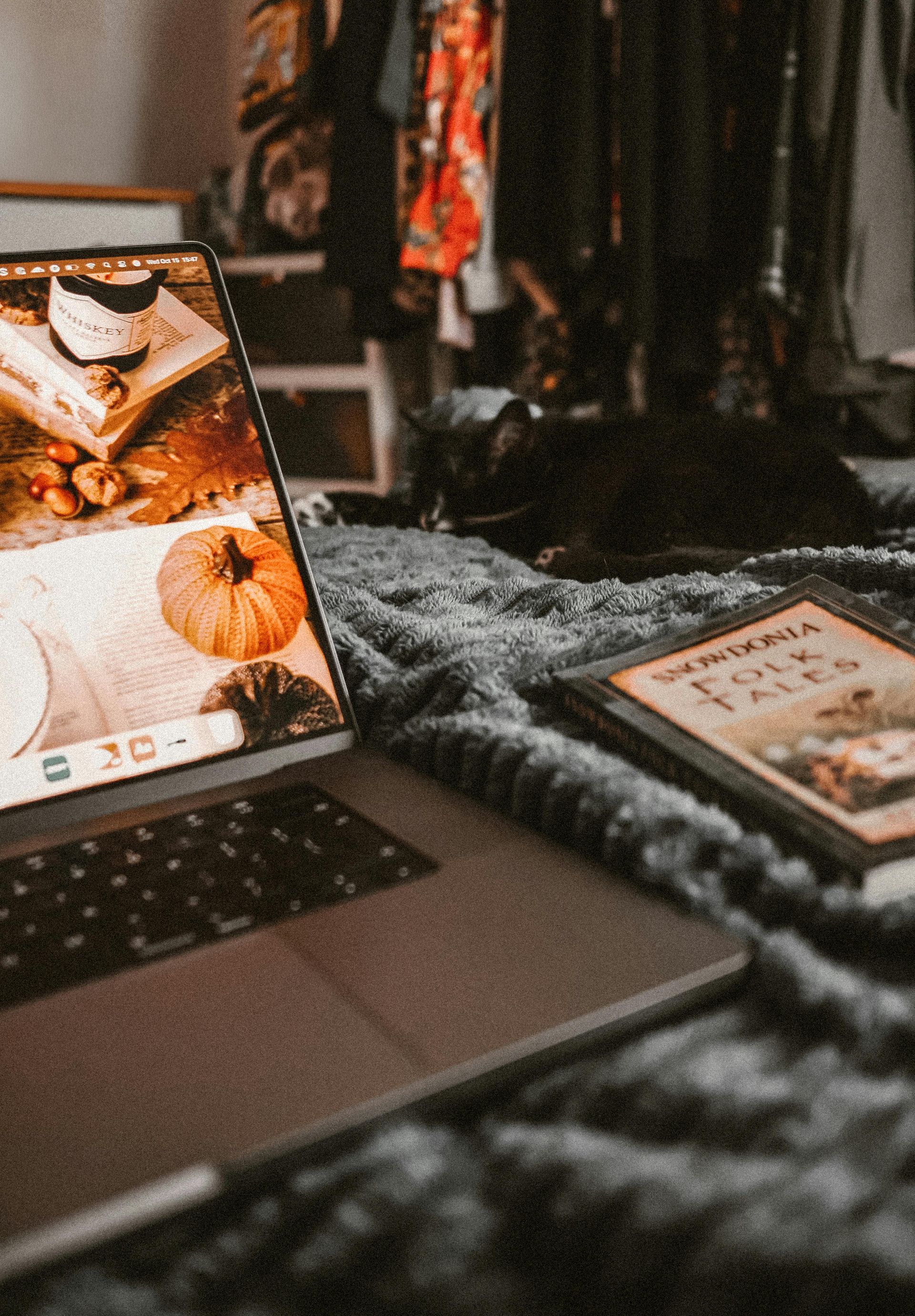 Laptop on a fuzzy blanket beside a smartphone, with clothes hanging in the background.