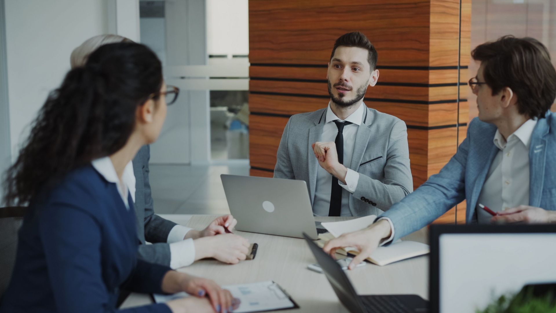 Business meeting with three coworkers discussing around a laptop in a modern office.