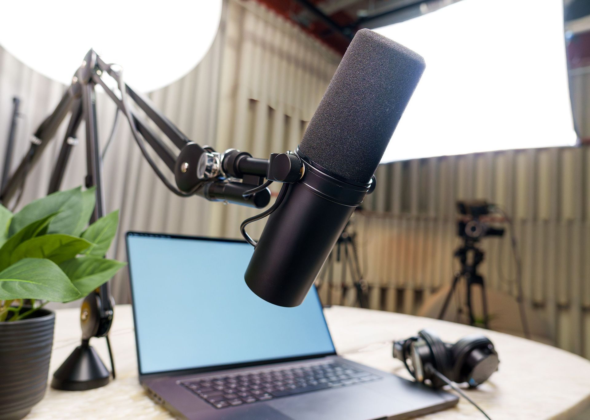 Podcast setup with boom mic, laptop, headphones, and plant on a desk