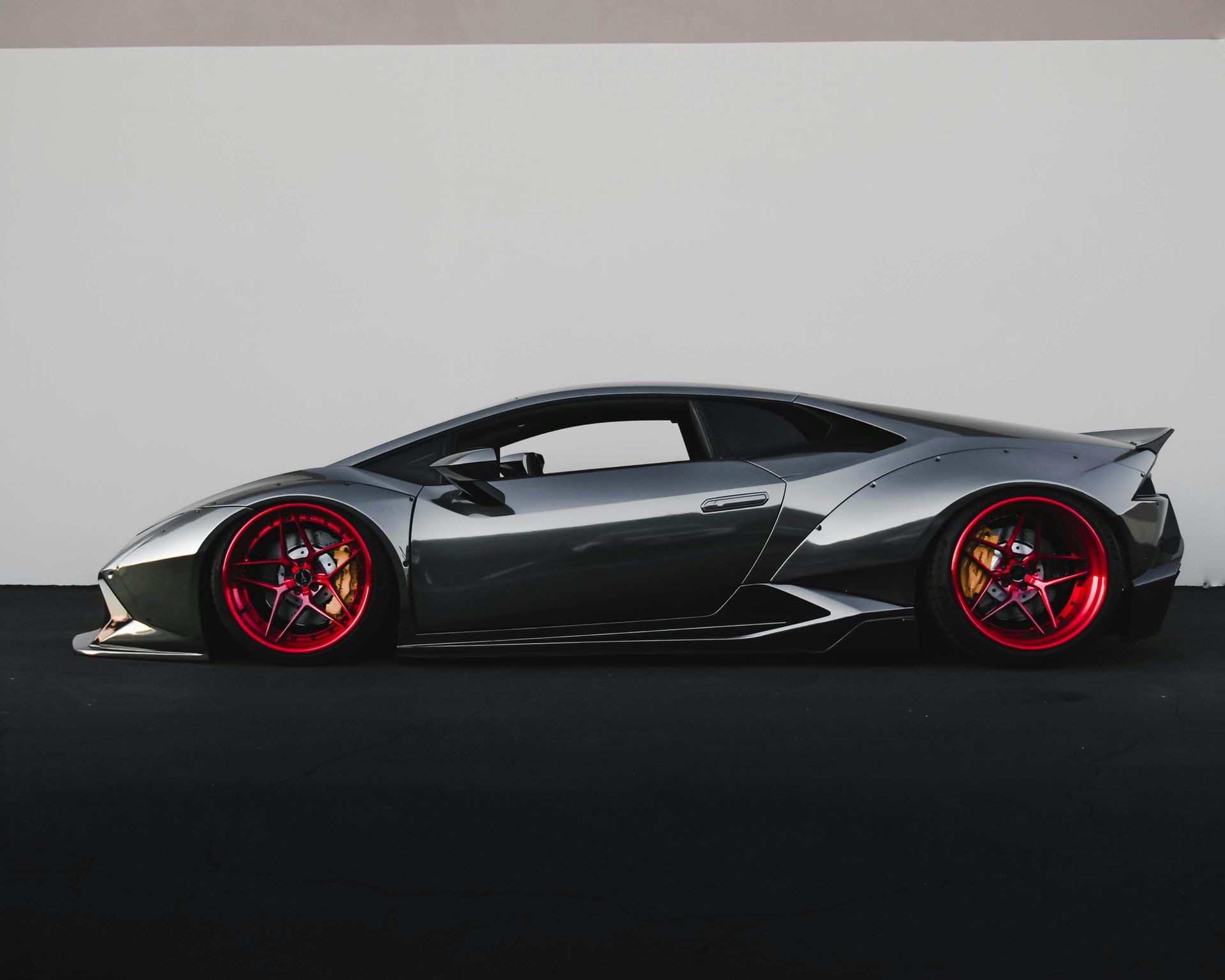 Black sports car with red rims on a dark studio background, side view