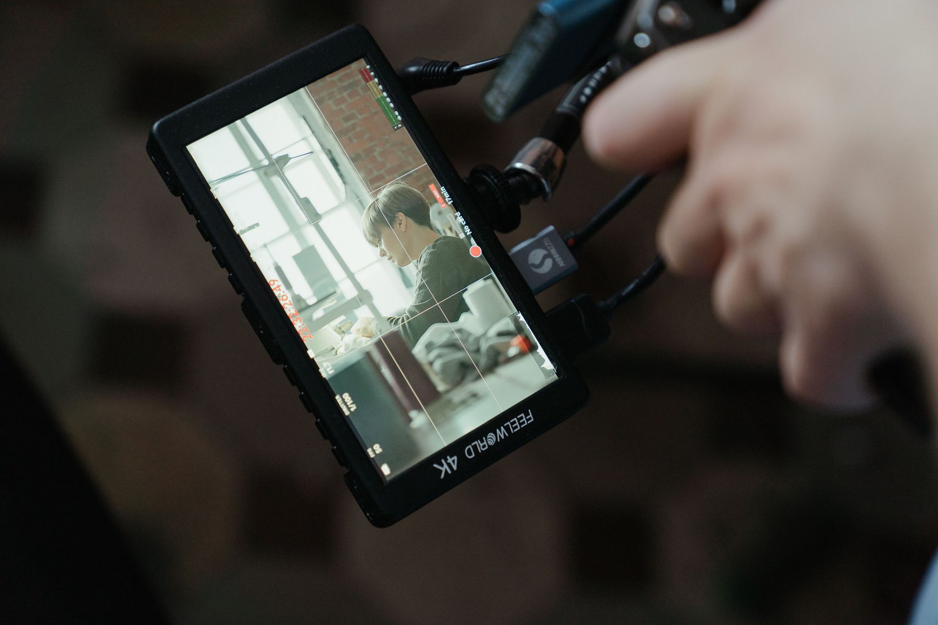 Camera monitor showing a person seated indoors, with a hand adjusting the equipment beside it