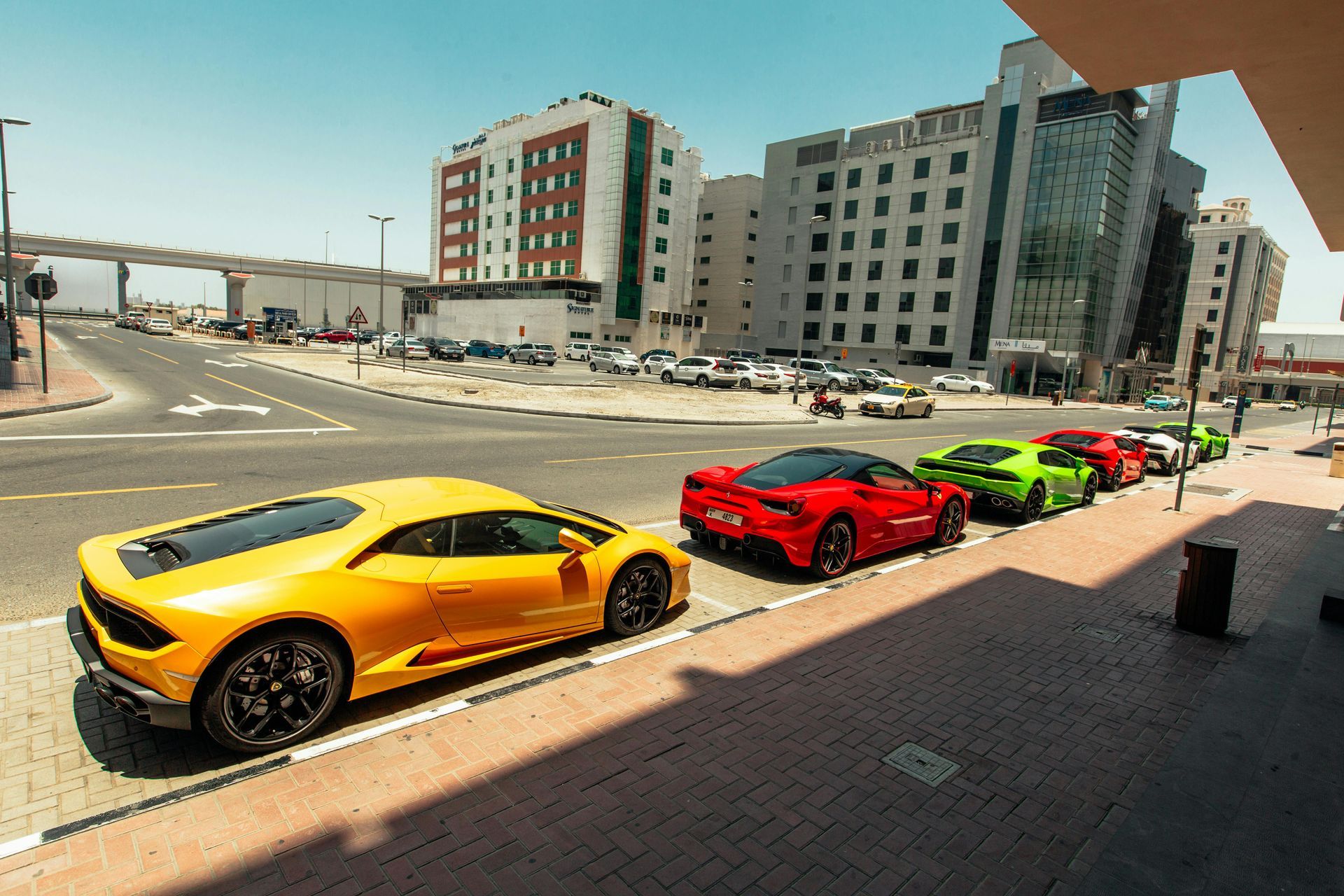 Yellow, red, and green sports cars parked along a city street beside tall buildings.