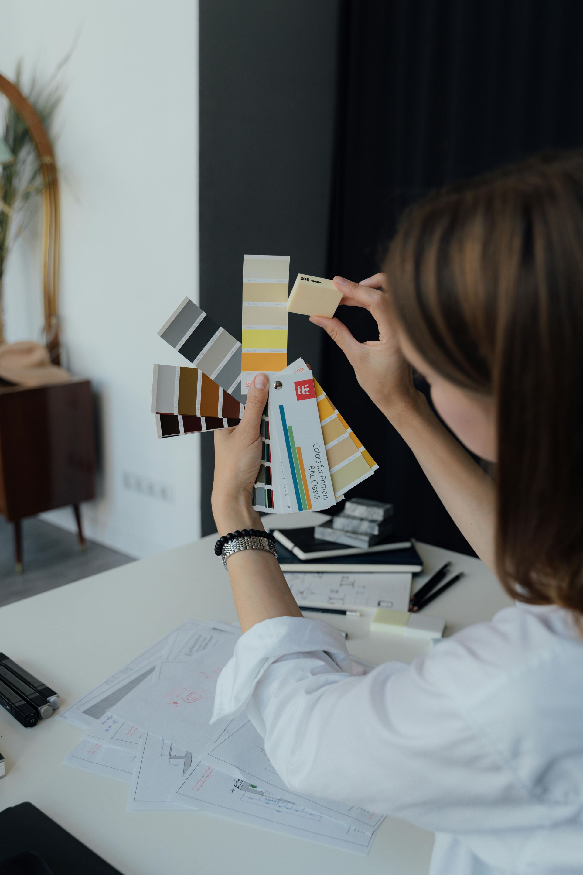 Designer comparing paint swatches at a desk with sketch plans and fabric samples