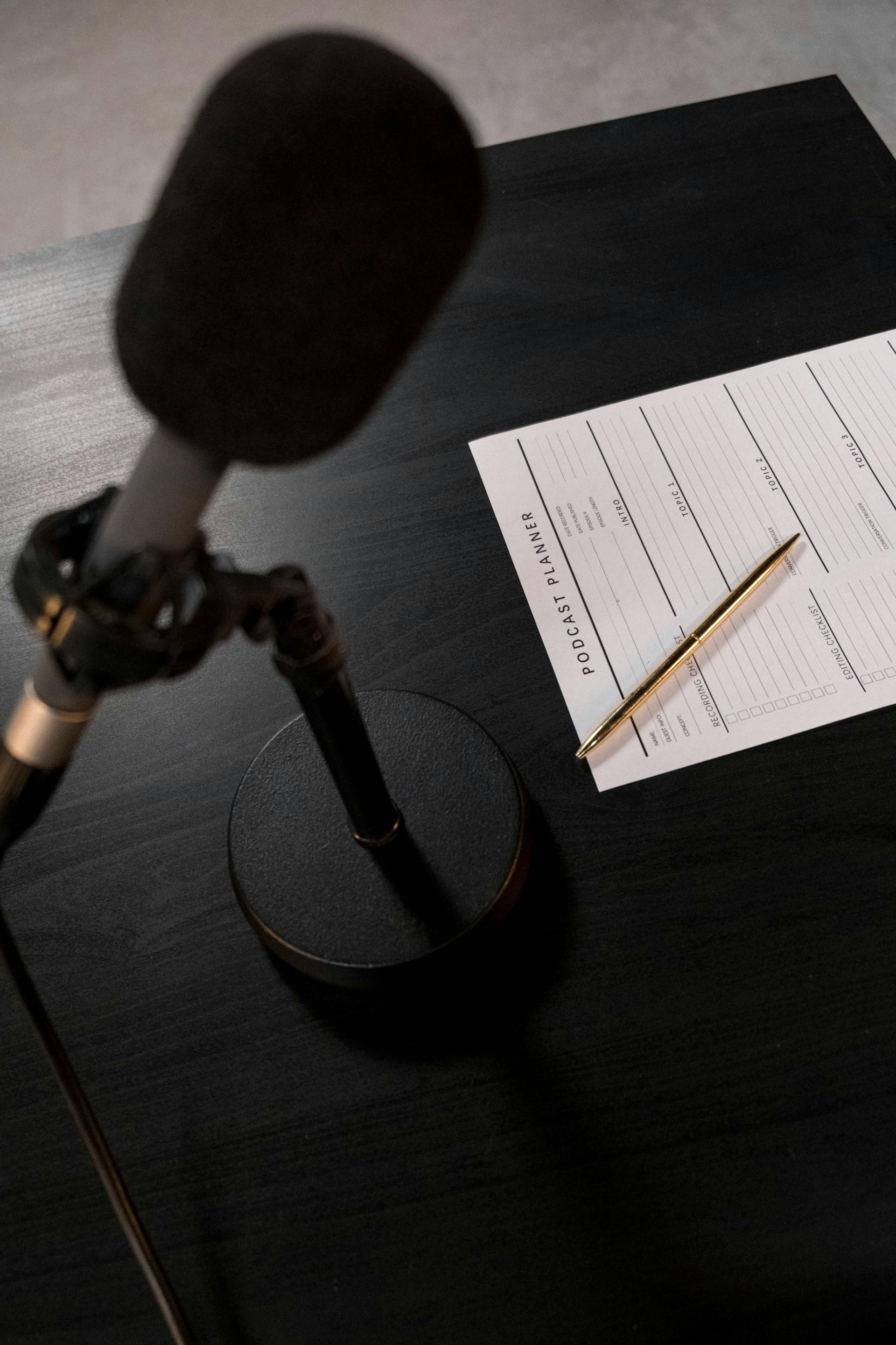 Desk microphone beside a sheet of music paper and pencil on a black table.