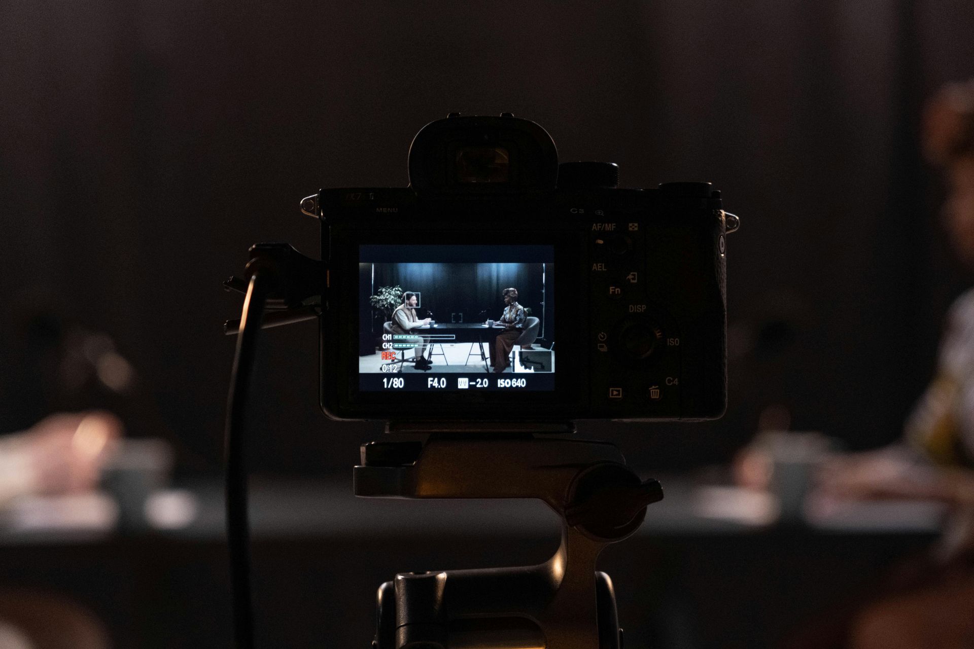 Camera filming a panel discussion in a dimly lit conference room