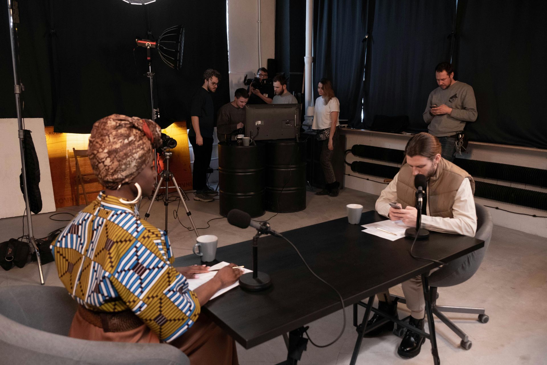 Panel discussion in a studio, with one speaker at a table and several people seated in the background.