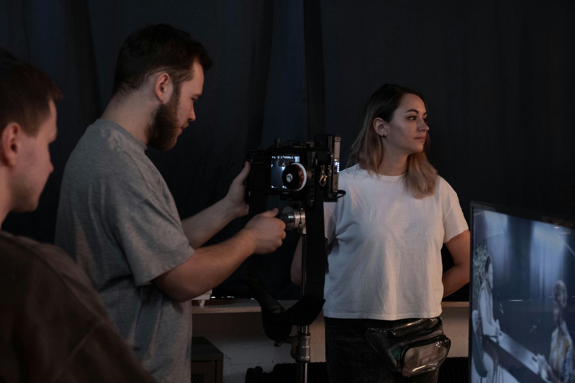 Film crew filming a woman indoors, with a camera rig and monitor in a dim studio