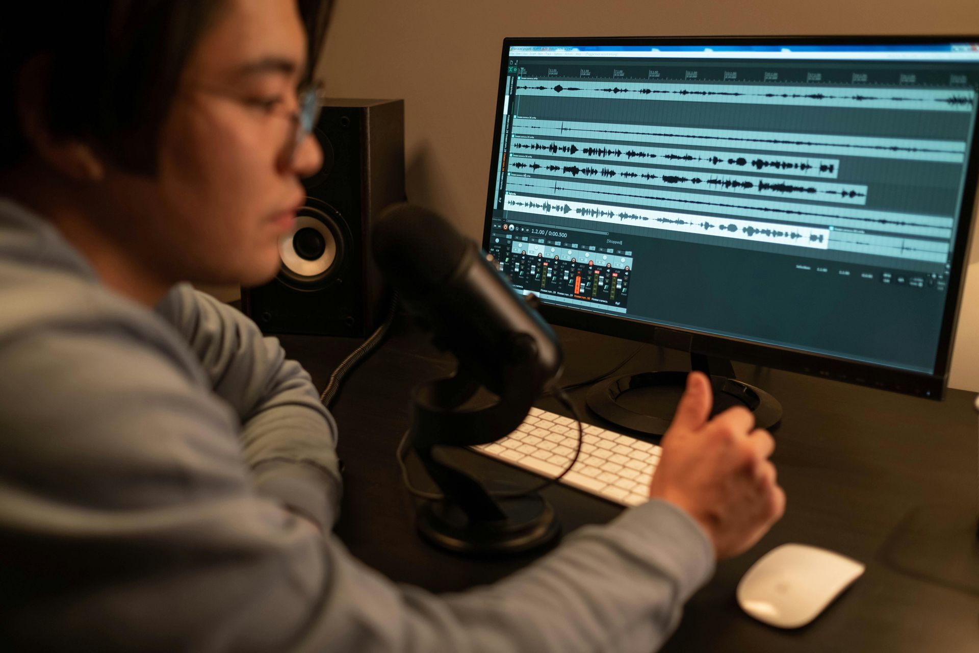 Person speaking into a microphone while editing audio on a computer monitor at a desk