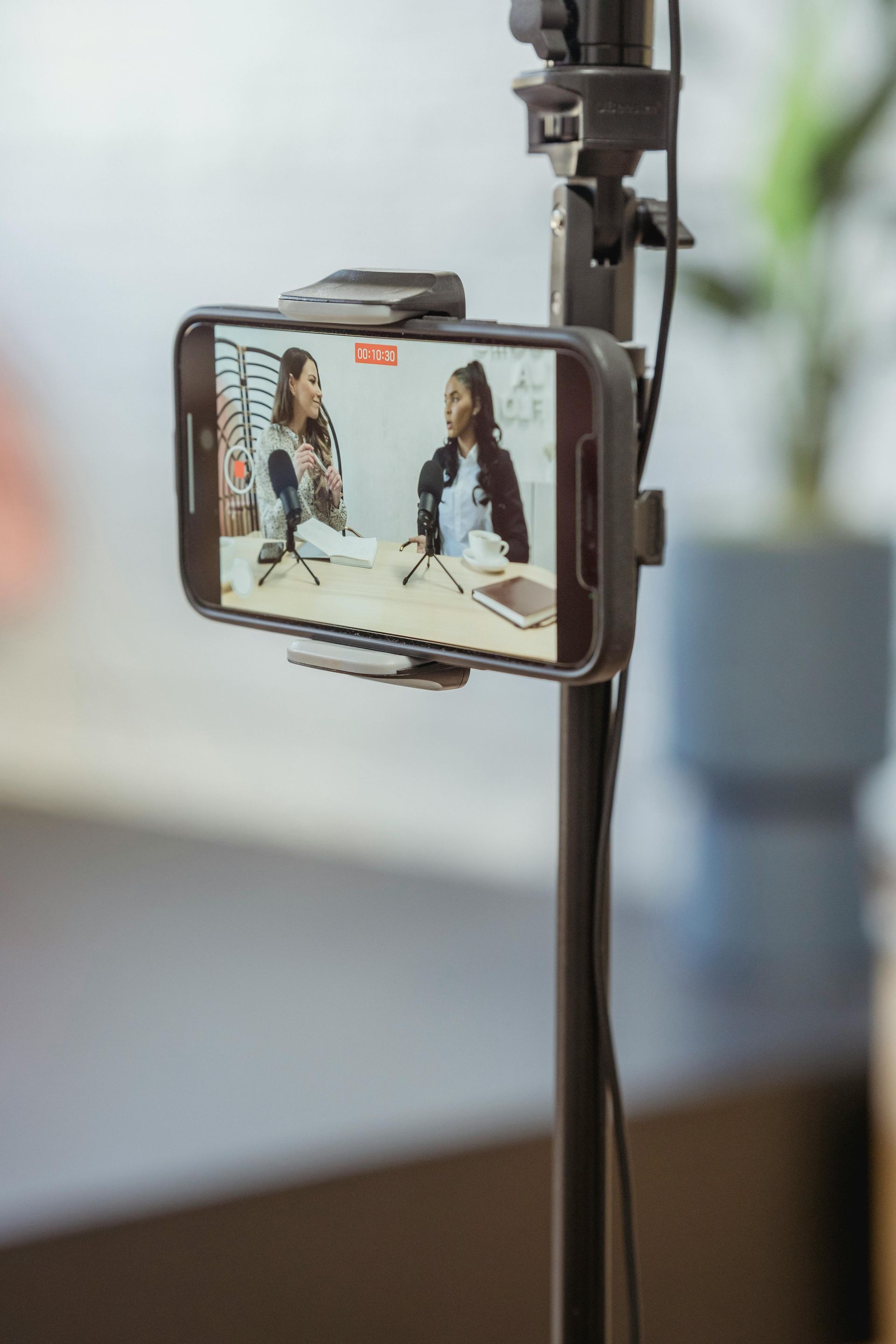 Smartphone mounted on a stand, showing a video of two people seated on a couch.