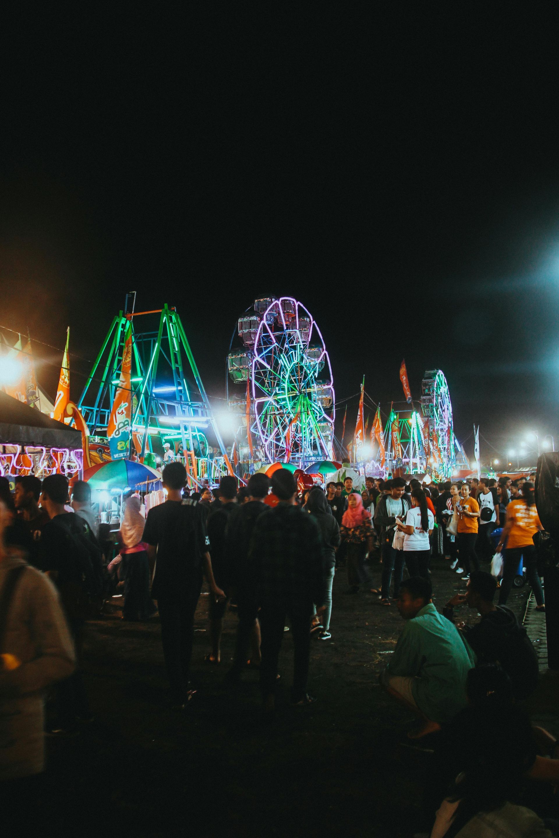 Nighttime fairground with colorful Ferris wheel and rides, crowded with people under bright lights