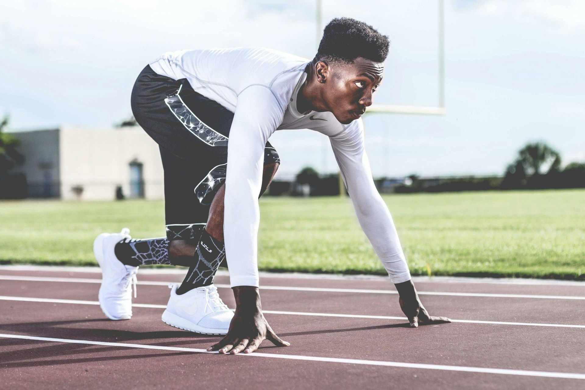 Sprinter crouched at the starting line on a track, wearing white and black athletic gear.